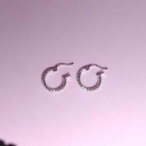 May include: A pair of silver hoop earrings with a textured, diamond-like pattern.