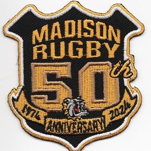May include: Embroidered patch in a shield shape, with the text "MADISON RUGBY 50 ANNIVERSARY" in gold and black. The patch includes the years 1974 and 2024, and a bulldog graphic. The border is white.