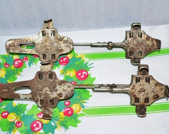 May include: A pair of vintage ice skate blades with metal frames and rusty metal plates. The blades are attached to each other with a metal bar.