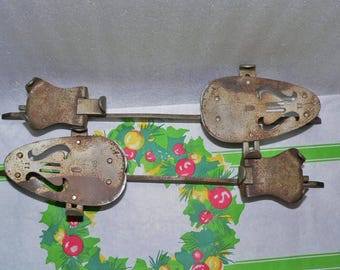 May include: A pair of vintage metal ice skate attachments. The attachments are rusty and have a decorative design. The attachments are connected by a metal bar.