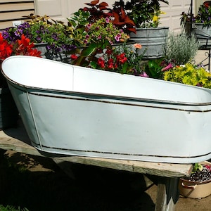 May include: A white oval metal basin with a smooth finish and a thin gold-toned rim detail along the top and bottom edges. The basin features a deep, elongated shape with slightly flared sides and a flat base, designed for holding various items.