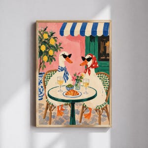 Peut inclure: Une impression d'art encadrée représentant deux canards blancs portant des lunettes de soleil noires assis à une table de bistrot ronde. Un canard porte une écharpe rayée bleue, l'autre un foulard à pois rouges. Vin, croissant et fleurs sur la table.