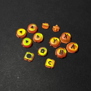 May include: A selection of orange and yellow game controller buttons. The buttons are in various shapes, including circles, squares, and directional pads. Some buttons are labelled with letters such as "A", "B", "C", "X", and "Y".