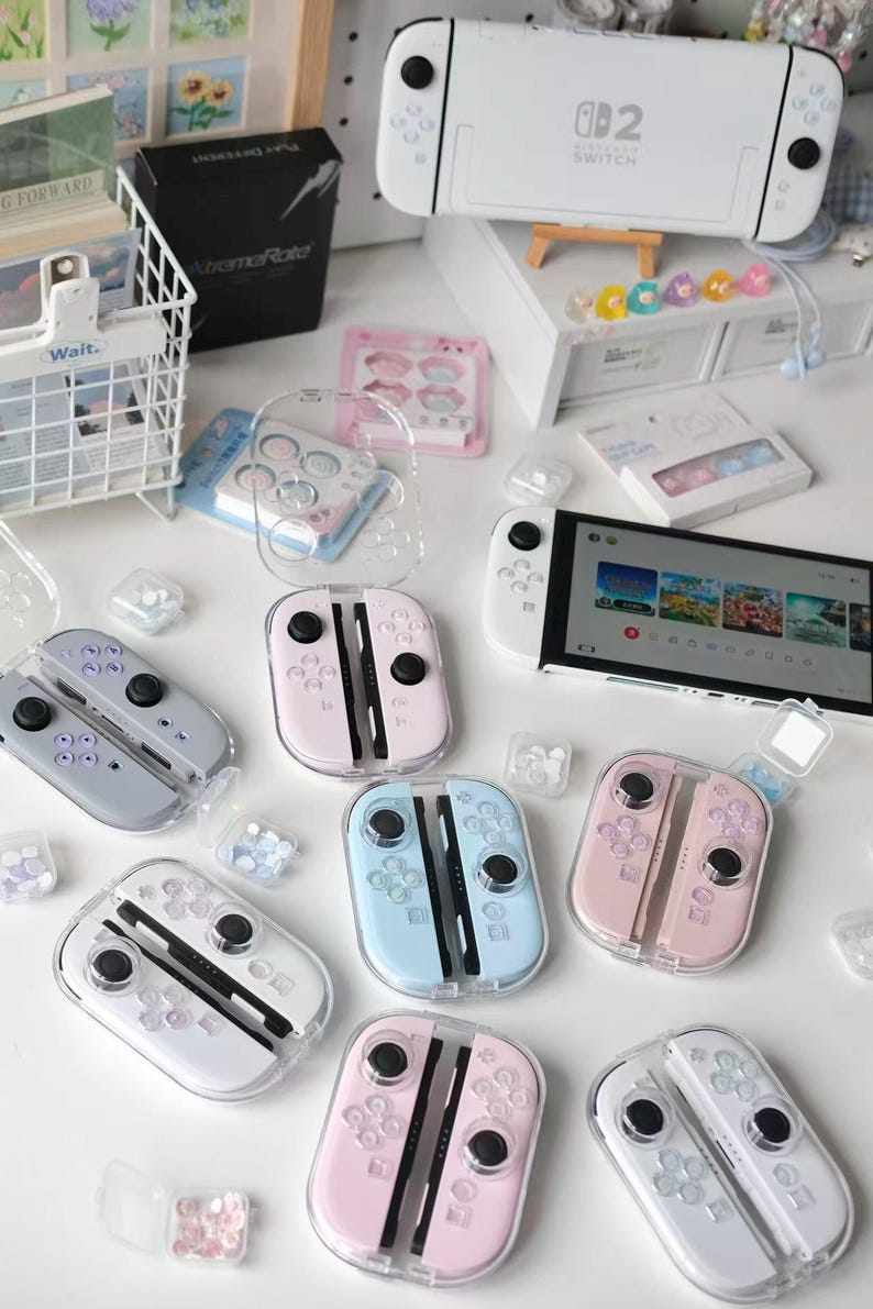 May include: A selection of pastel-coloured Nintendo Switch accessories, including Joy-Cons in pink, blue, and grey, alongside a white Switch console. Clear protective cases and small decorative items are also present, creating a playful aesthetic.