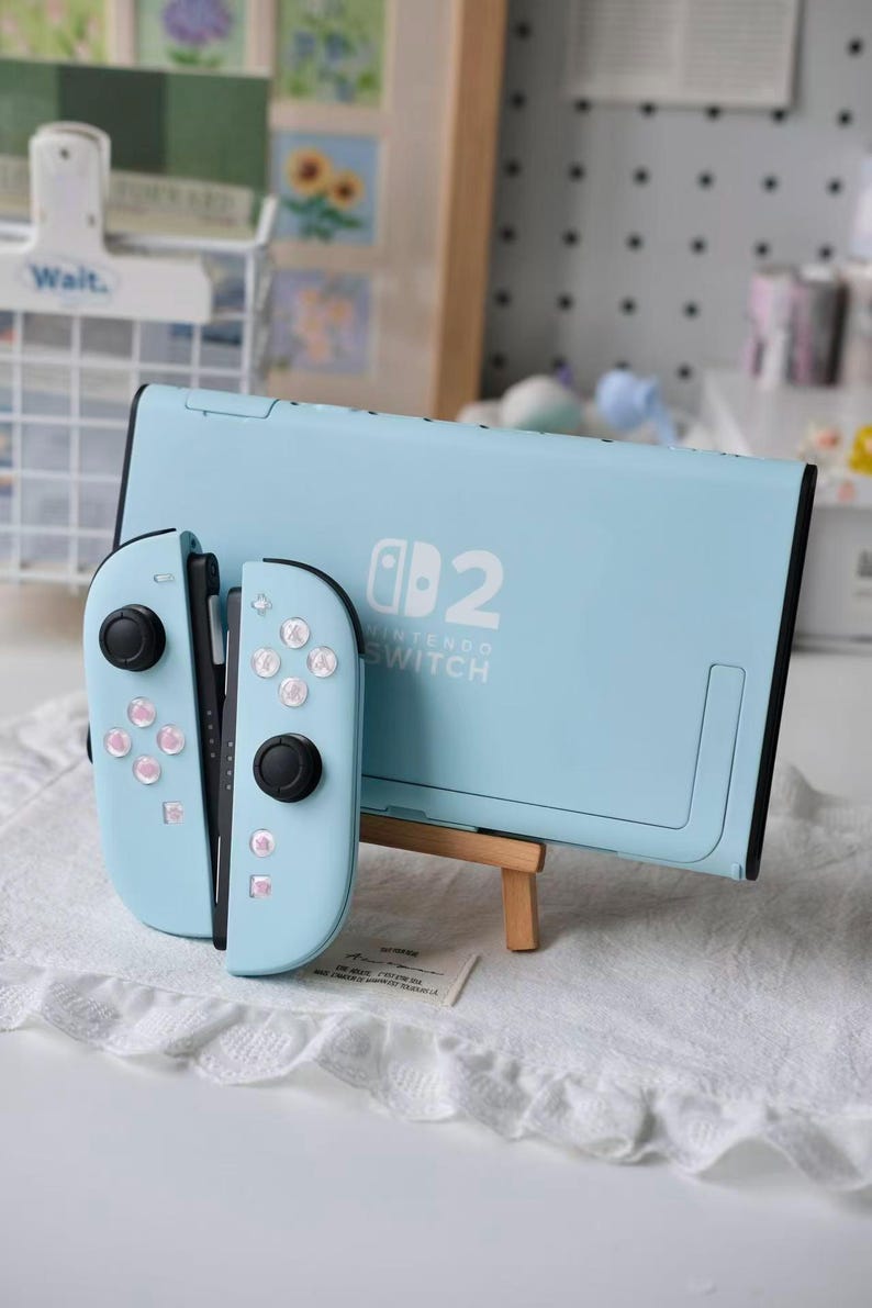 May include: A light blue Nintendo Switch console and two matching Joy-Con controllers. The console features the white Nintendo Switch logo and the number 2 on the back. The controllers have light blue shells with black joysticks and buttons.