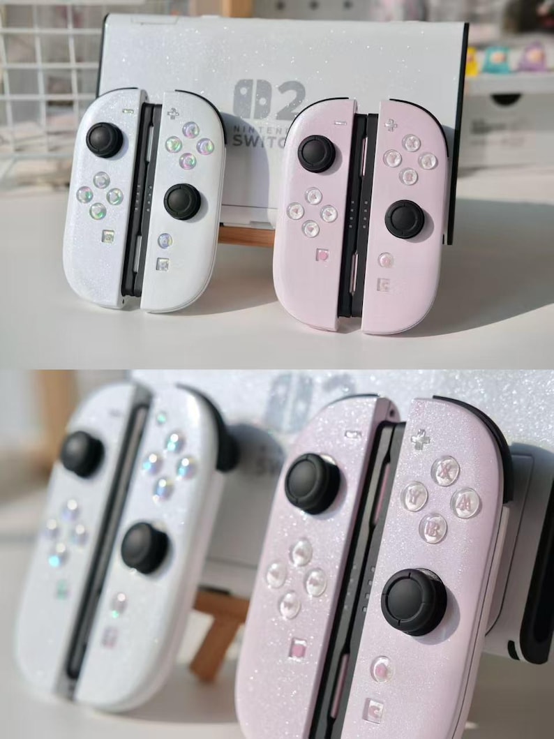 May include: Two sets of Nintendo Switch Joy-Con controllers. One set is white with iridescent buttons, the other is pink. Both sets have black control sticks and a glittery finish. A Nintendo Switch console is in the background.