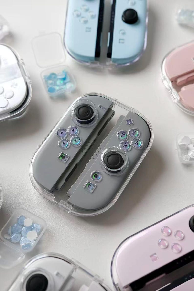 May include: Various game controllers in grey, light blue, and pink, each encased in a clear protective shell. The controllers feature black joysticks and colourful button layouts. Small clear containers hold blue and clear decorative elements.