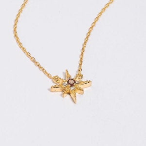 May include: A gold chain necklace with a star-shaped pendant featuring a small brown gemstone in the centre and smaller clear gemstones around it.