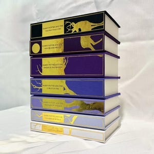 May include: A stack of seven Harry Potter books with gold lettering and illustrations on the spines. The books are arranged from largest to smallest, with the top book being "Harry Potter and the Deathly Hallows".