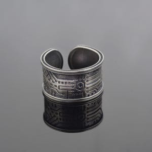 May include: A silver ring featuring a circuit board design. The ring is wide and has a textured finish.