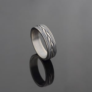 Puede incluir: Un anillo de banda de plata con un diseño trenzado.