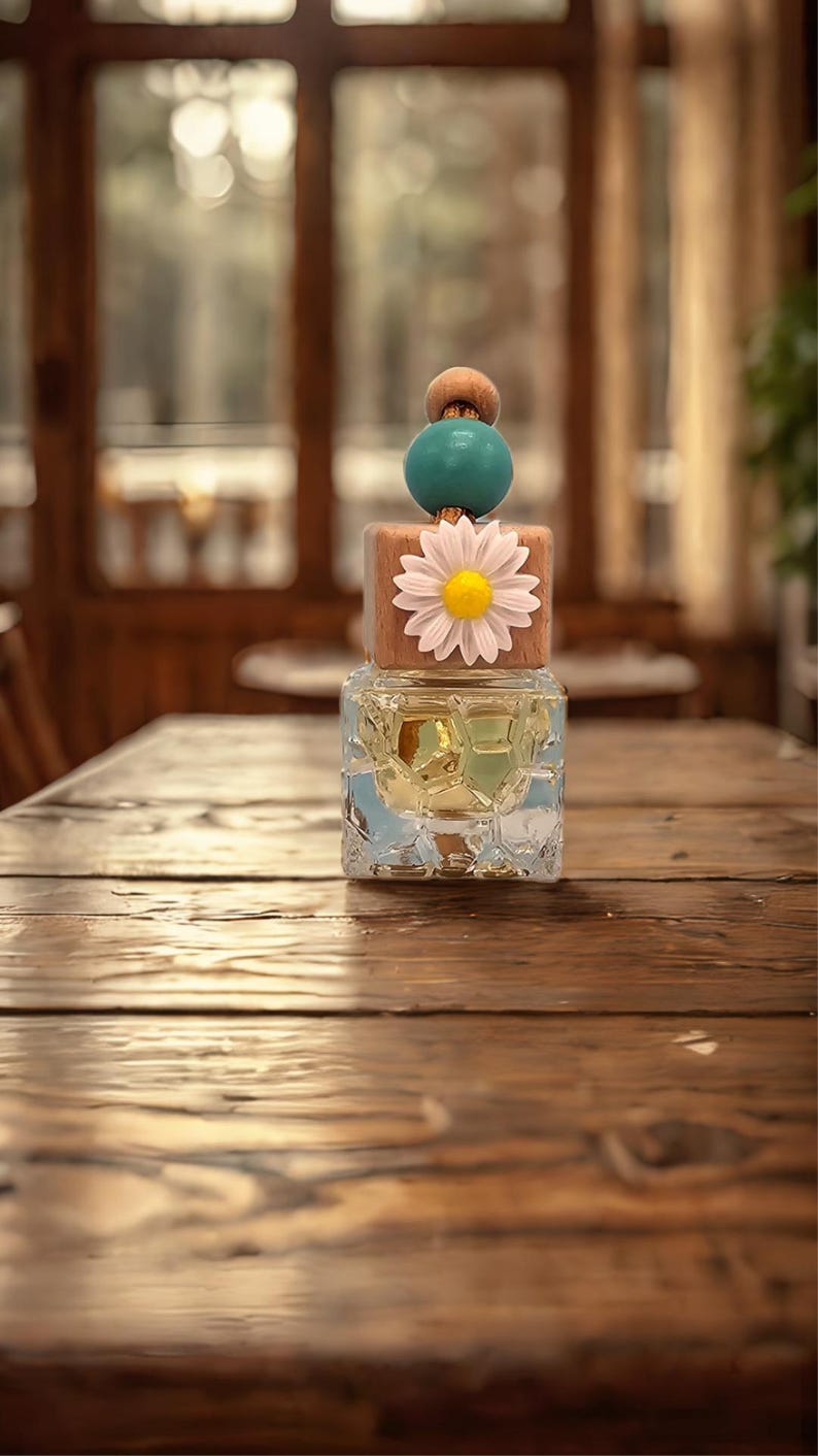 May include: A clear glass bottle with a textured surface and a wooden lid with a white daisy and blue and brown beads. The bottle is sitting on a wooden table.
