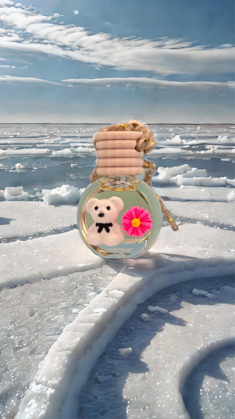 K&ouml;nnte beinhalten: Ein transparenter Glas-Lufterfrischer f&uuml;r das Auto mit einer rosa Blume und einem wei&szlig;en Teddyb&auml;ren im Inneren. Der Lufterfrischer h&auml;ngt an einer braunen Schnur.