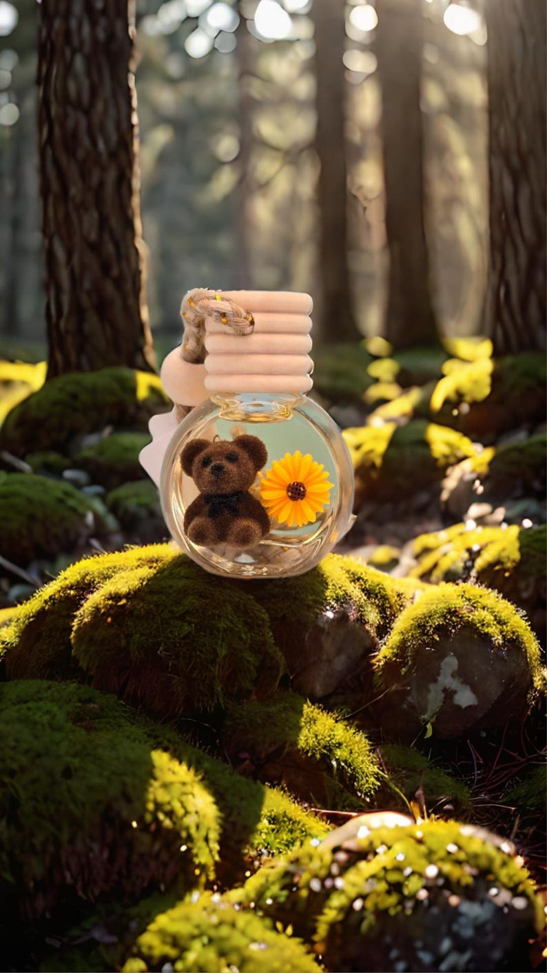 May include: A clear glass car air freshener with a brown teddy bear and a yellow flower inside. The air freshener is hanging from a brown rope and has a wooden ring on top.