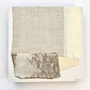May include: Abstract art piece with a beige, brown, and white color scheme. The piece is made of layered fabric and has a textured surface. The artist's signature, "Gray", is in the bottom right corner.