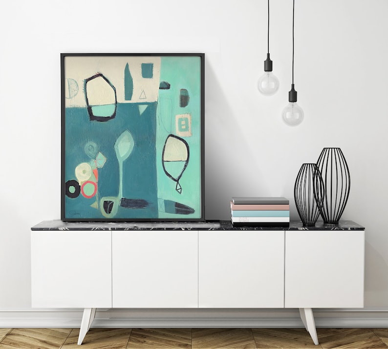 May include: Abstract painting in shades of blue, green, and white with geometric shapes and lines. The painting is framed in black and displayed on a white cabinet with a black marble top.