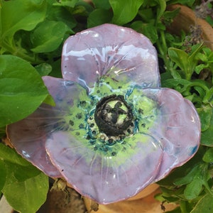 May include: A ceramic flower with a purple and green glaze. The flower has a detailed center with a black and green design.