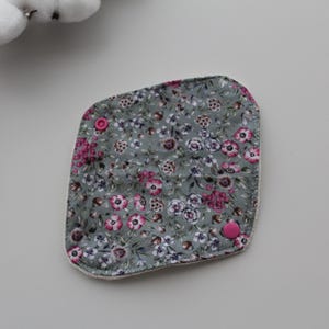 May include: A square, floral-patterned reusable pad with a gray background and pink and white flowers. The pad has two pink snaps and a white border. The pad is made of soft fabric.