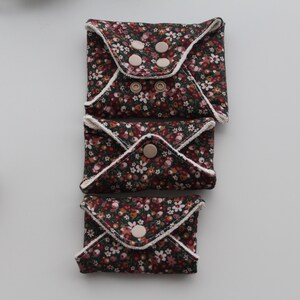 May include: Three reusable cloth pads with a floral pattern in shades of brown, red, and white. Each pad is folded and secured with snaps. The pads are arranged vertically on a white surface.