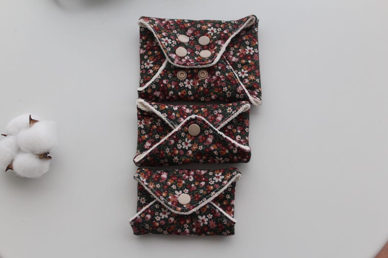 May include: Three reusable cloth pads with a floral pattern in shades of brown, red, and white. Each pad is folded and secured with snaps. The pads are arranged vertically on a white surface.