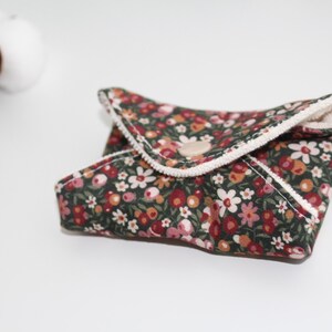 May include: A floral patterned, reusable cloth pad with a dark green background and a variety of flowers in shades of red, pink, and white. The pad is folded and secured with a wooden button.
