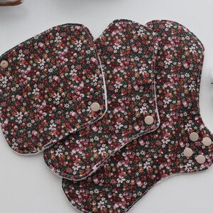 May include: Reusable cloth menstrual pads in a floral pattern. The pads are dark brown with a small white and pink floral print. The pads have snap closures and are in various shapes and sizes.