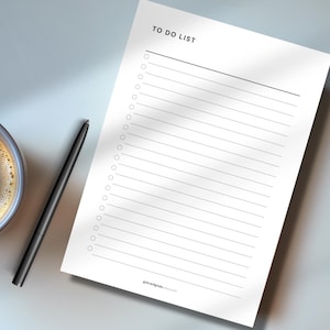 May include: A white To Do List notepad with a black pen and a cup of coffee. The notepad has a header that reads "TO DO LIST" and includes lines and circles for check boxes. The pen is black and the coffee cup is dark brown.