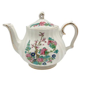 May include: A white porcelain teapot with a ribbed body and a matching lid. The teapot features a colorful floral pattern with pink, blue, and green botanical designs. The spout, handle, and lid finial are accented with gold trim.