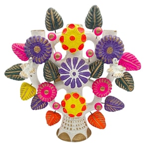 May include: A white ceramic tree of life sculpture featuring vibrant hand-painted flowers in yellow, purple, and pink. The structure includes dark green and orange leaves, small pink spheres, and two white bird figures perched on the branches.