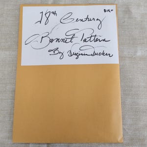 May include: A tan paper envelope with a white rectangular label attached to the front. The label features handwritten black ink text that reads 18th Century Bonnet Pattern By Virginia Tucker, with the handwritten price $15.00 in the top right corner.