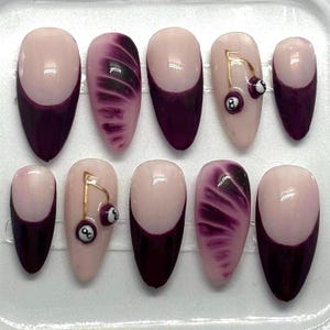 Puede incluir: Conjunto de diez uñas postizas con un diseño degradado en rosa y morado. Algunas uñas tienen un encanto de cereza dorada con una bola negra de 8 en la parte superior.