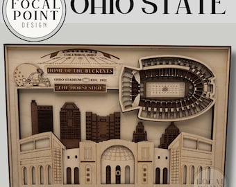 Może przedstawiać: Wielowarstwowa drewniana dekoracja ścienna przedstawiająca stadion Ohio Stadium oraz panoramę Columbus. Projekt zawiera napis Home of the Buckeyes, Ohio Stadium Est. 1922 oraz The Horseshoe, a także grafikę kasku futbolowego i widok stadionu.