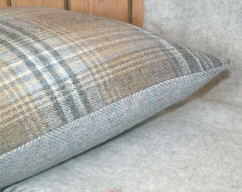 May include: A gray and brown plaid throw pillow with a light blue border. The pillow is sitting on a light gray throw blanket.