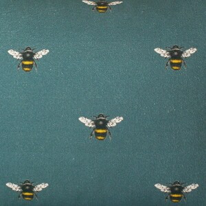 May include: Teal fabric with a repeating pattern of black and yellow bumblebees.
