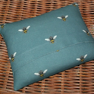 May include: A teal blue pillow with a repeating pattern of black and yellow bees. The pillow has a flap on the back to insert a pillow insert.