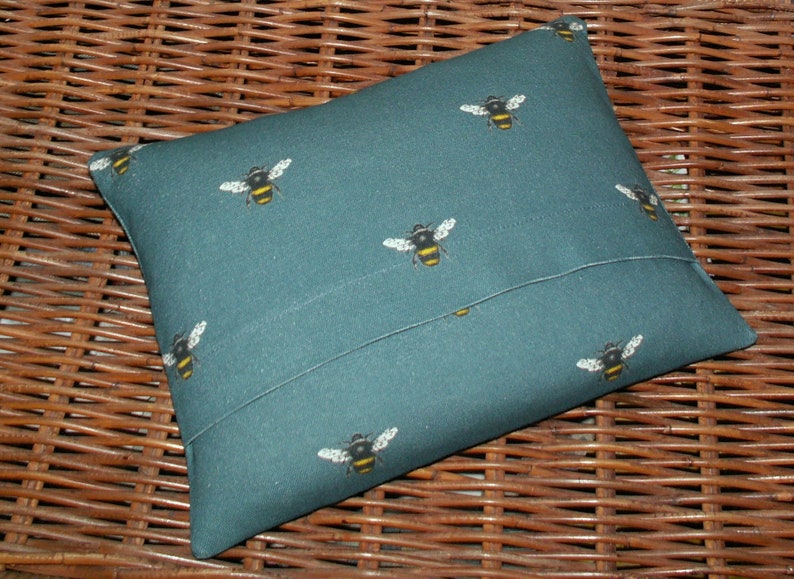 May include: A teal blue pillow with a repeating pattern of black and yellow bees. The pillow has a flap on the back to insert a pillow insert.