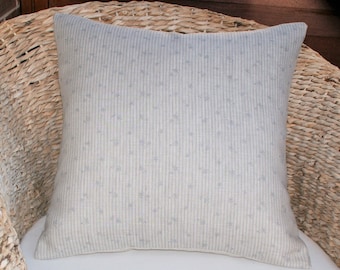 May include: A light gray throw pillow with a white and gray striped pattern and a subtle floral design. The pillow is sitting on a wicker chair.