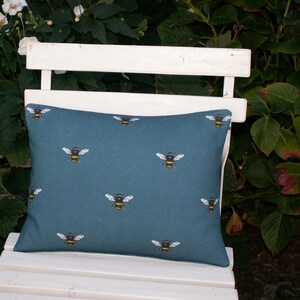 May include: A teal blue throw pillow with a repeating pattern of yellow and black bumblebees. The pillow is sitting on a white wooden bench.