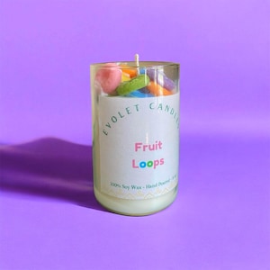 May include: A clear glass candle jar with a white label that says "Evolet Candle" and "Fruit Loops". The jar is filled with a white candle and colorful fruit loop cereal.