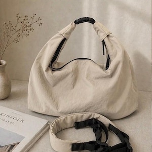 Puede incluir: Un bolso estilo hobo de color beige hecho de una tela ligera y arrugada. El bolso cuenta con una abertura superior asegurada por una hebilla de pl&aacute;stico negra. Se incluye una correa de hombro acolchada a juego con correas de nailon negro.