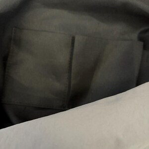 Puede incluir: El interior de un bolso negro con un forro de tela suave y un bolsillo abierto rectangular cosido en el panel posterior. El bolsillo est&aacute; dividido en dos secciones por una costura vertical, proporcionando espacio para guardar objetos peque&ntilde;os.