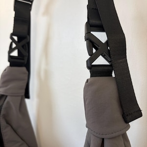 Puede incluir: Un bolso gris con correas de nailon negro ajustables conectadas por hebillas de pl&aacute;stico negro de liberaci&oacute;n lateral. La tela del bolso es lisa y mate, con las correas fijadas de forma segura a las esquinas superiores de la estructura.