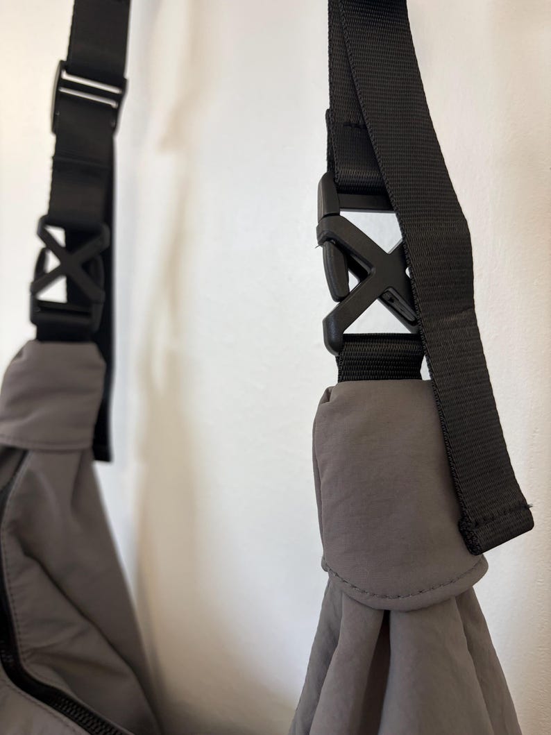 Puede incluir: Un bolso gris con correas de nailon negro ajustables conectadas por hebillas de pl&aacute;stico negro de liberaci&oacute;n lateral. La tela del bolso es lisa y mate, con las correas fijadas de forma segura a las esquinas superiores de la estructura.