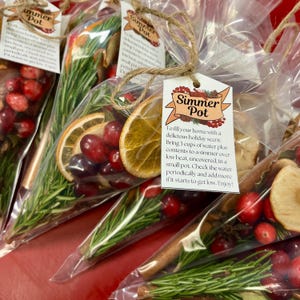 Könnte beinhalten: Ein Set aus vier durchsichtigen Plastiktüten, gefüllt mit Zutaten für einen Simmertopf. Die Tüten enthalten Orangenscheiben, Cranberries, Rosmarinzweige, Zimtstangen und Apfelscheiben. Jede Tüte hat ein Etikett mit der Aufschrift "Simmer Pot" und Anweisungen zur Verwendung.