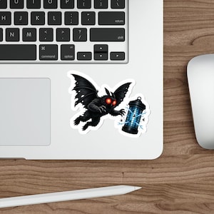 May include: A die-cut sticker featuring a dark, furry creature with large, glowing red eyes and expansive wings, reaching toward a blue electric bug zapper lantern that is surrounded by small flying insects and bright white electrical sparks.