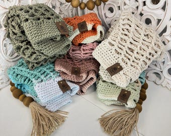May include: A collection of crocheted baby hats in various colors, including green, blue, pink, and orange. Each hat has a brown leather tag with the text "Little & Loved" on it. The hats are arranged on a white surface with a wooden bead garland.