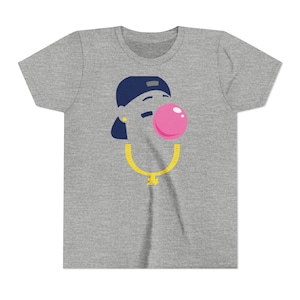 Puede incluir: Una camiseta gris con una ilustración de dibujos animados. El diseño incluye una gorra azul marino, una burbuja de chicle rosa y un collar de cadena dorada con un colgante. El gráfico está centrado en la camiseta.