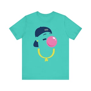 May include: Teal t-shirt featuring a cartoon face with a navy blue cap, a pink bubblegum bubble, and a gold chain necklace. The design is simple and bold, with a playful aesthetic. The shirt is made of a soft, comfortable material.