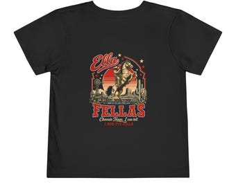 May include: A black short-sleeve t-shirt featuring a graphic print of a cowboy on a rearing horse against a red sun. The text reads Ella FELLAS, Home of the Ella Fella Club, Choosin Texas, I can tell, and the phone number 1-800-777-FELLA.
