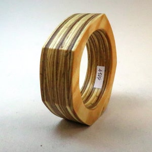 Könnte beinhalten: Ein Holzring in Hexagonform, hergestellt aus geschichtetem Holz mit natürlicher Oberfläche. Der Ring hat ein Etikett an der Seite mit der Aufschrift "4964".